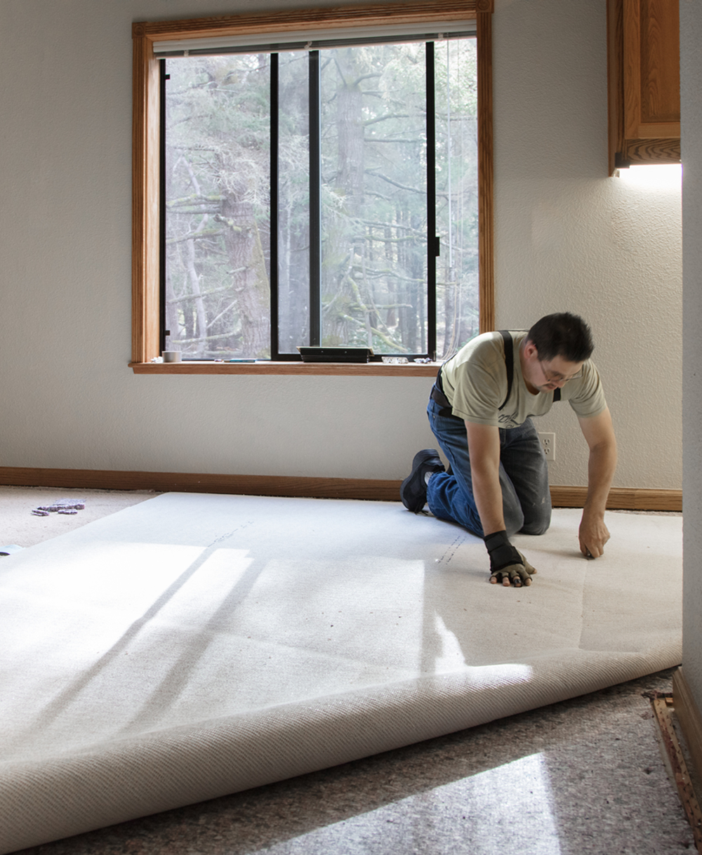 Worker laying white carpet by window.